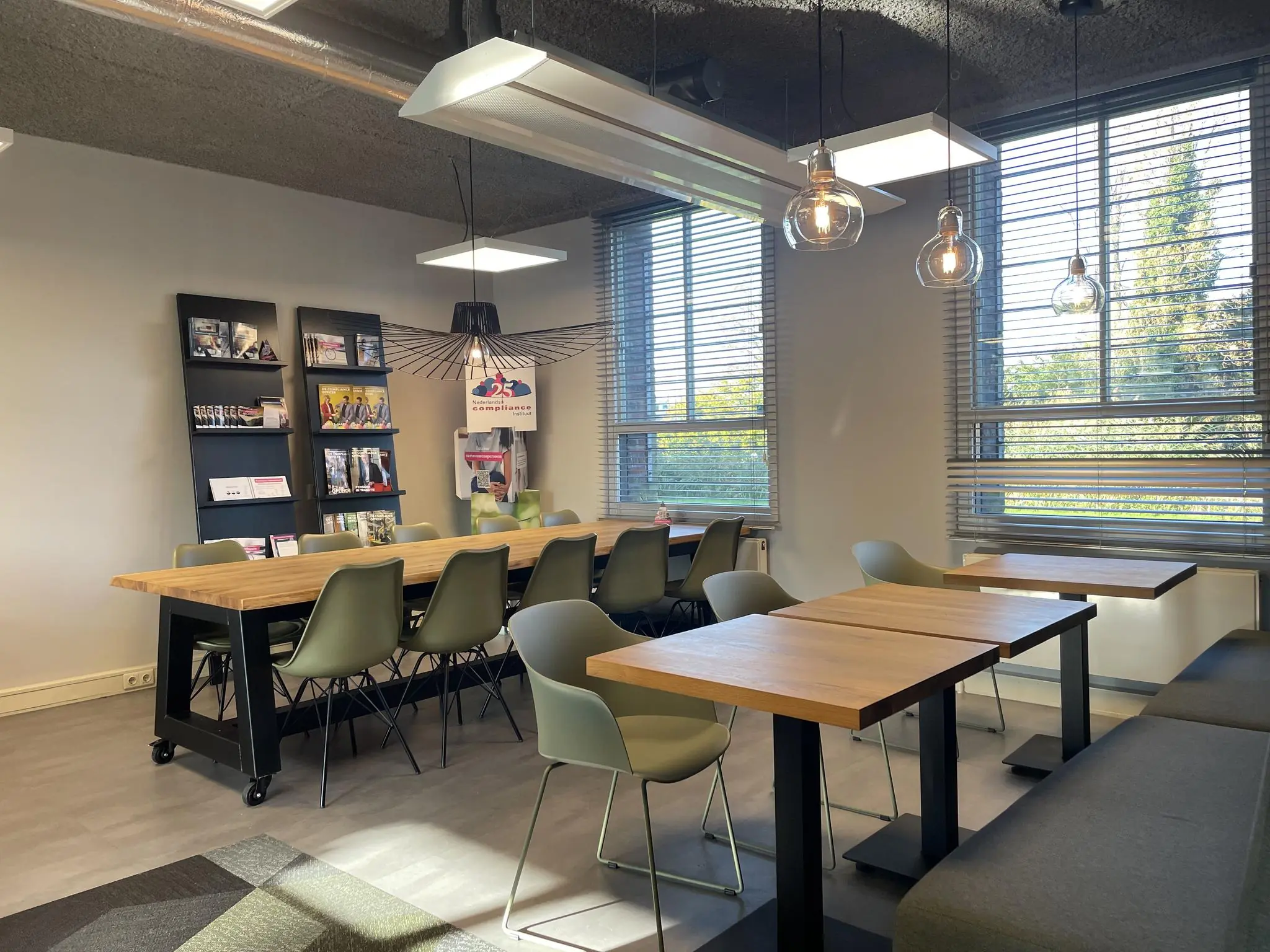 Moderne vergaderruimte aan de Jan Leentvaarlaan met houten tafels, groene stoelen en grote ramen met jaloezieën.